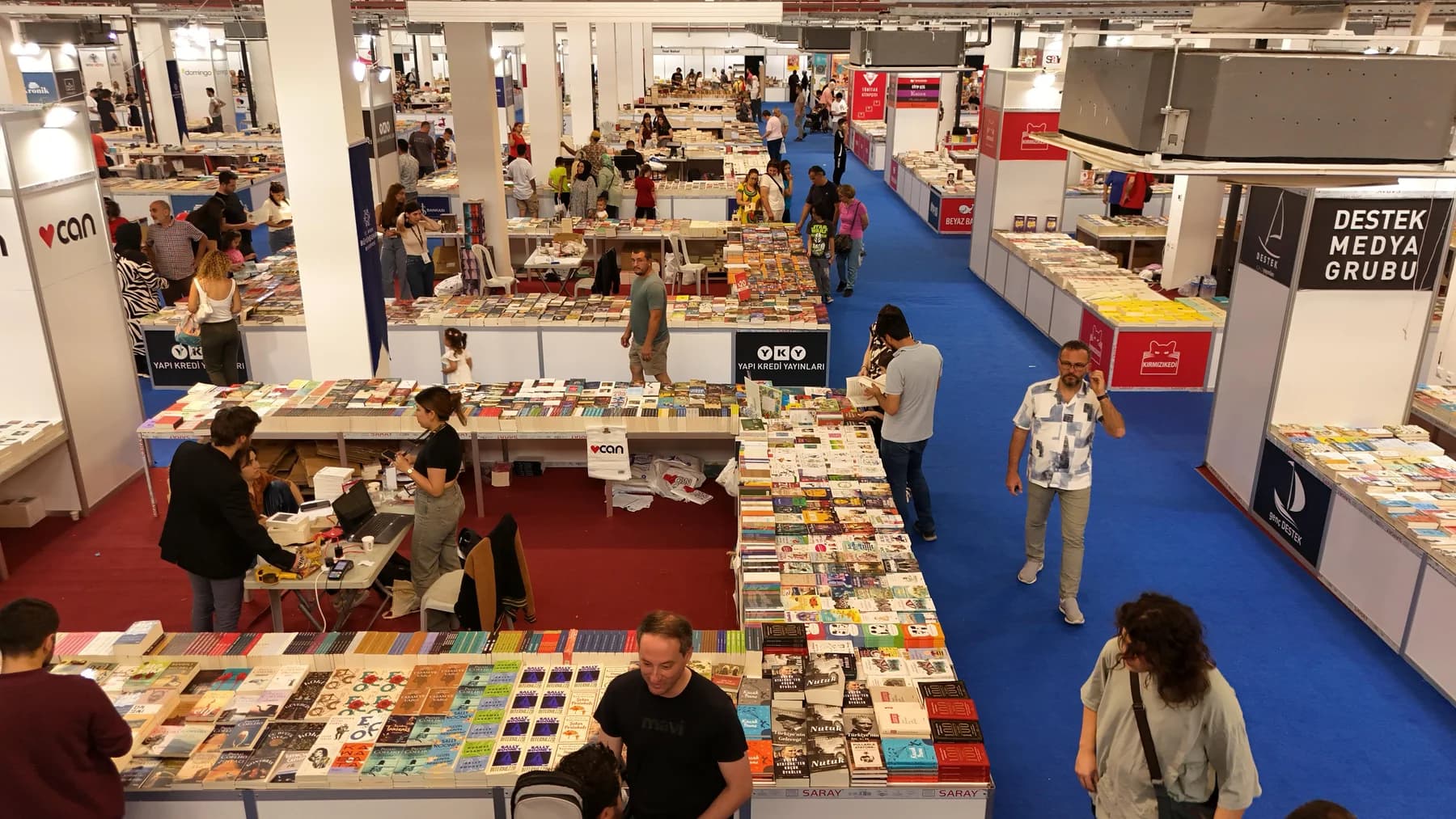 Fuar salonunun yukarıdan görünümü: mavi halılı koridorlar boyunca uzanan yayınevi stantları ve kitap masaları