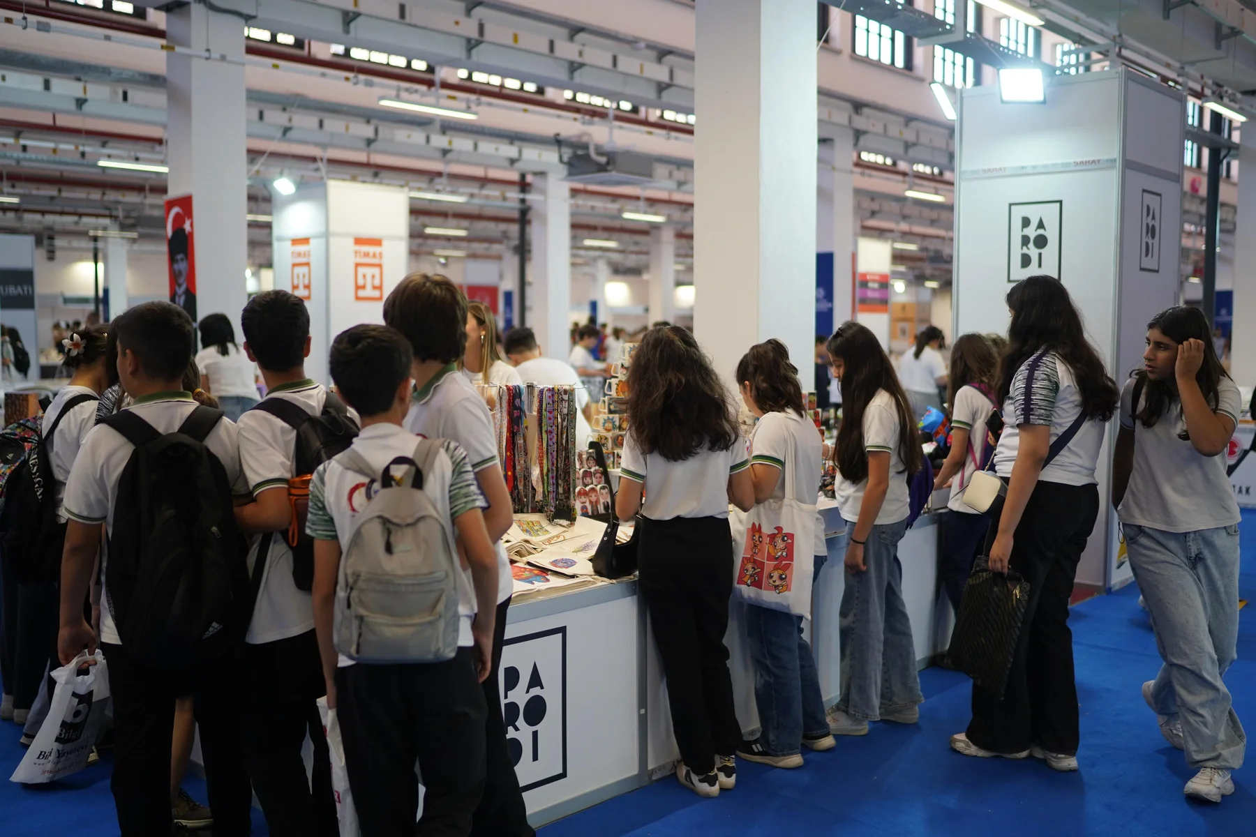 Okul üniformalı öğrencilerin bir stant tezgâhında ürünlere bakması