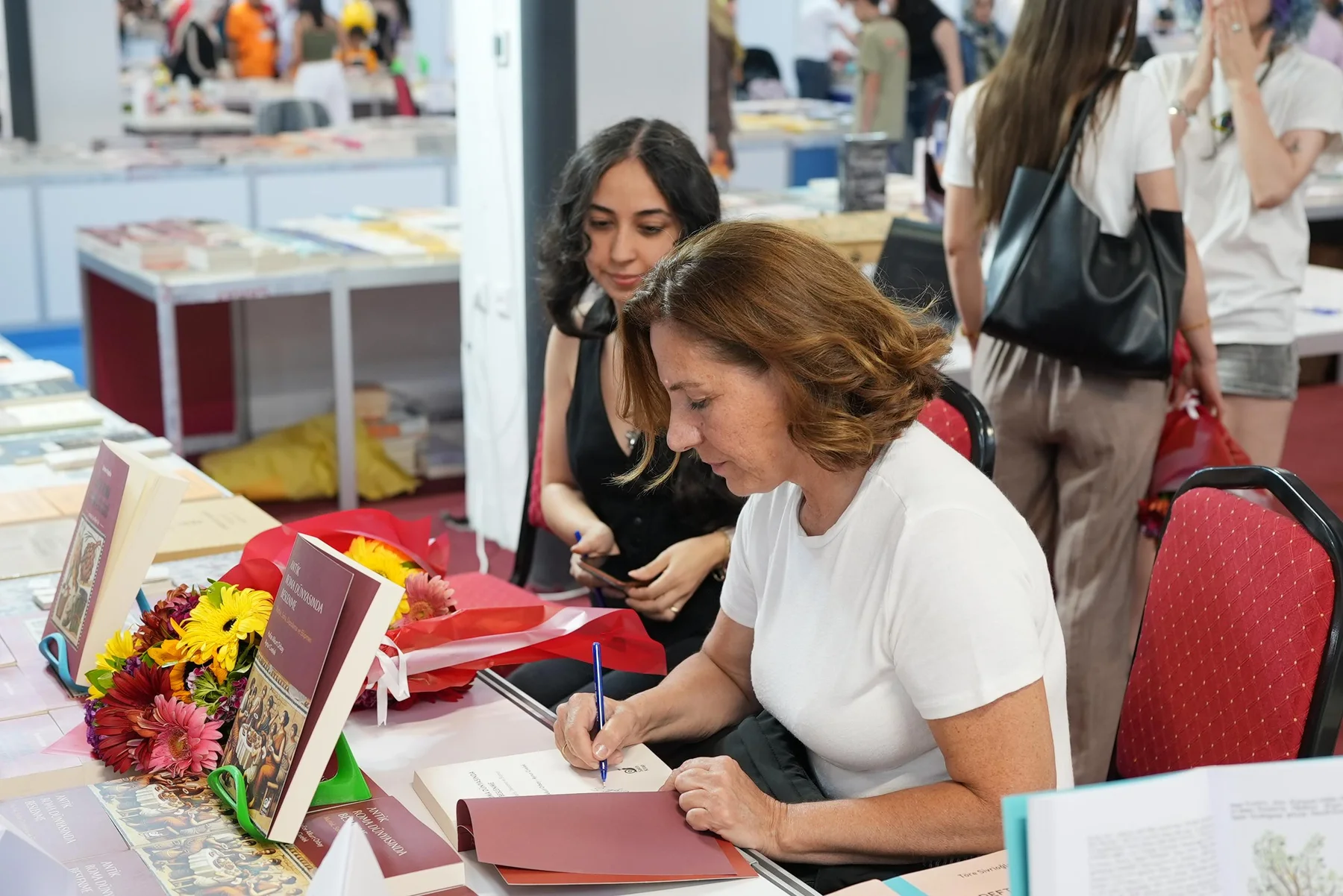 Bir yazarın masada kitap imzalaması, yanında bekleyen okur