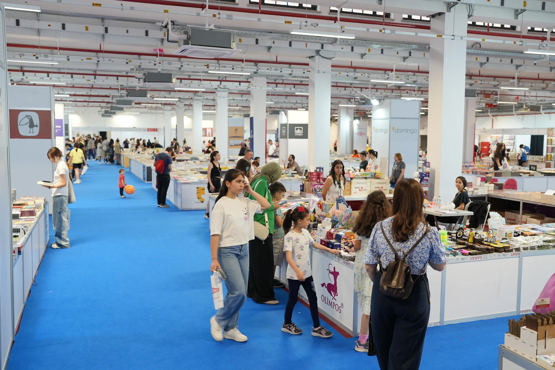 Salonun geniş koridorunda stantlar arasında gezinen aileler ve çocuklar