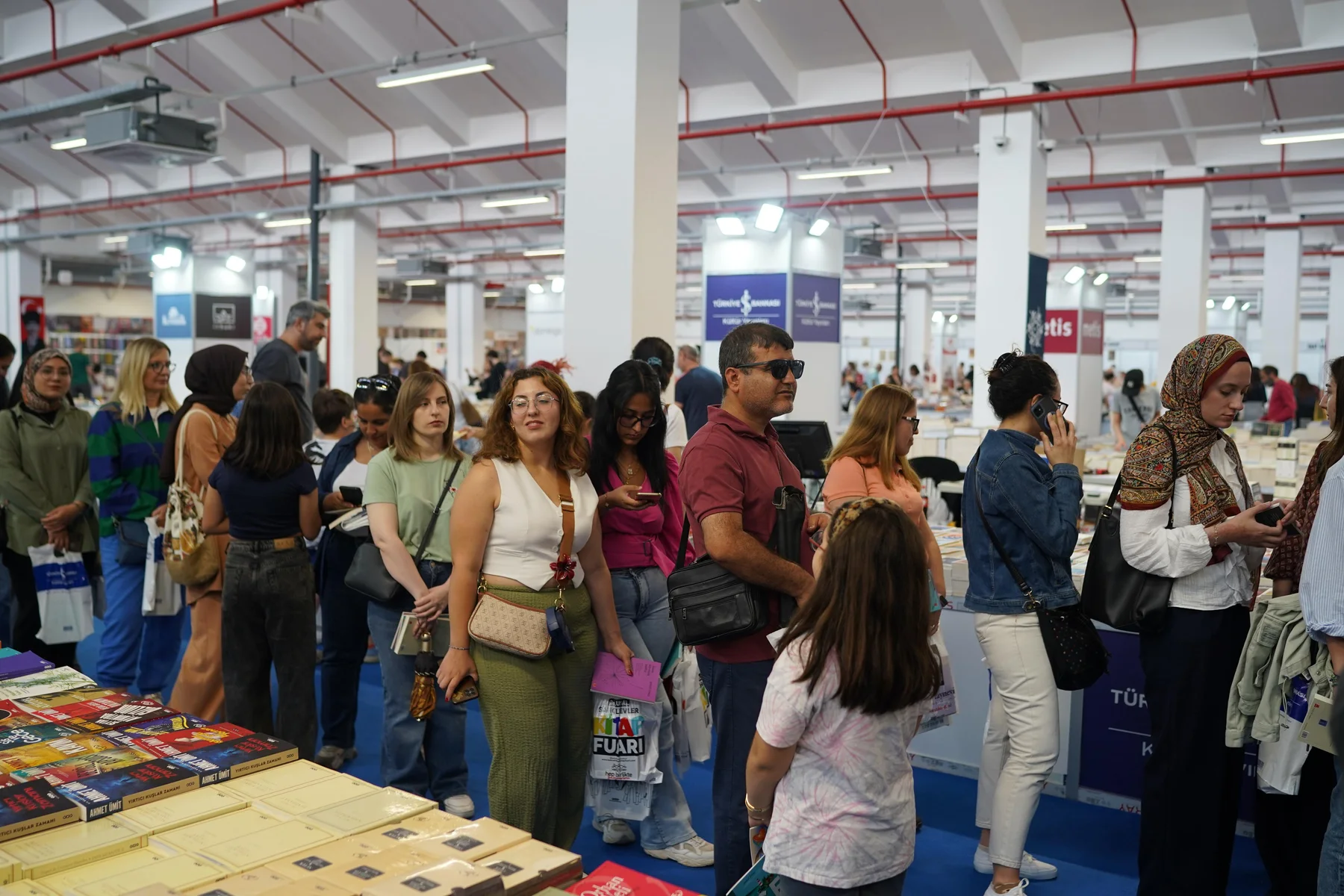 Kitap masalarının önünde bekleyen kalabalık bir ziyaretçi grubu