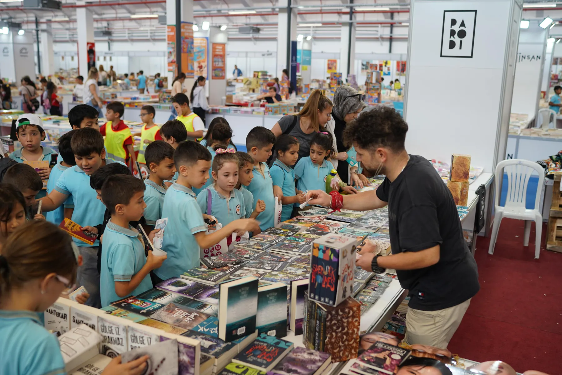 Okullarıyla gelen öğrencilerin bir kitap masasının çevresinde toplanması