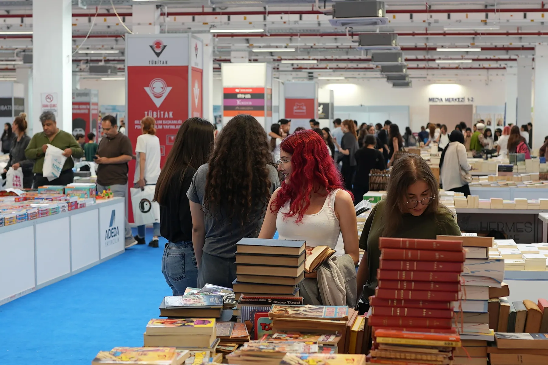 Bir yayınevi standında raflara ve masalara dizilmiş kitaplara bakan ziyaretçiler